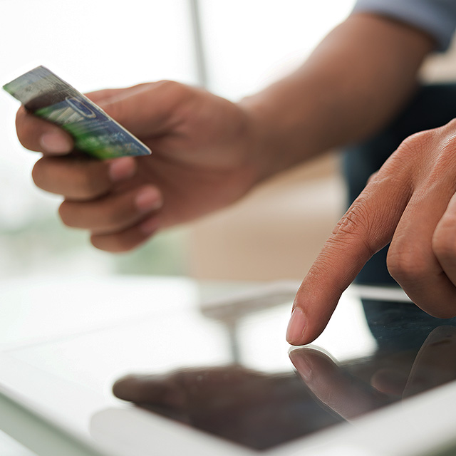Close up of man holding a mobile phone and credit card near a desktop