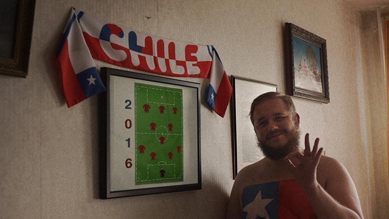 Football fan waving next to poster of 2016 football field layout with Chile banner above it.
