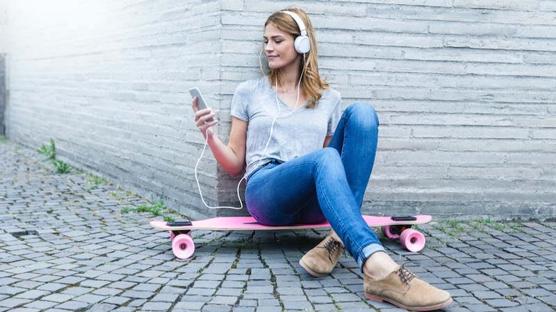 Woman sat on skateboard looking at her phone